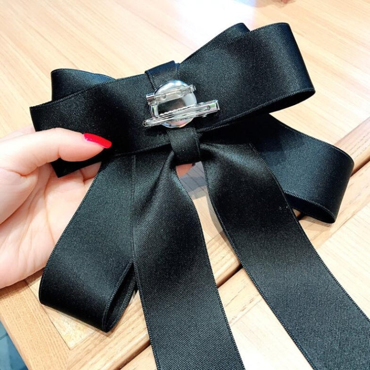 Black satin bow brooch detail with silver clasp pin and rhinestone pearl center.
