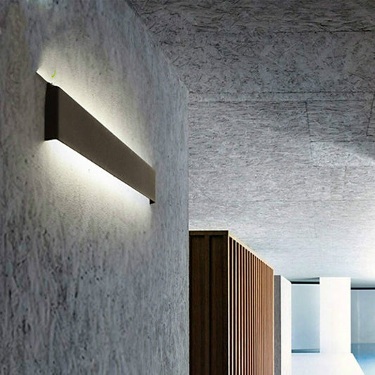 Black linear LED wall sconce with angled light strip on a stone wall.