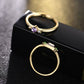 Gold-tone crystal rings on display box: purple center ring and green detail open ring