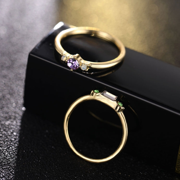 Gold-tone crystal rings on display box: purple center ring and green detail open ring