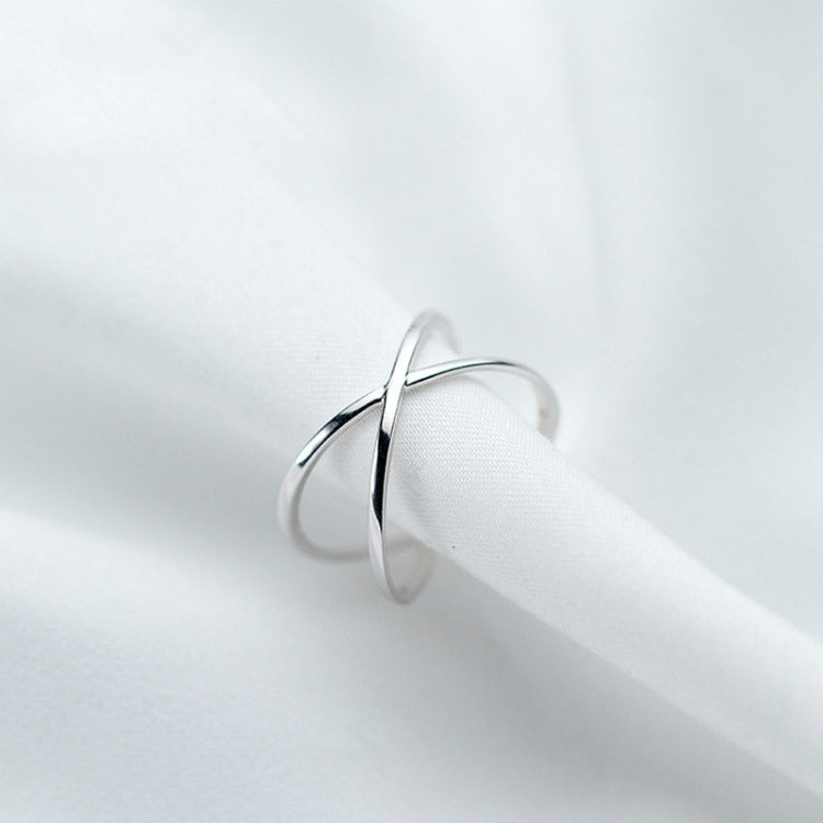 Sterling-silver tone open cross ring on a finger, minimal polished band.