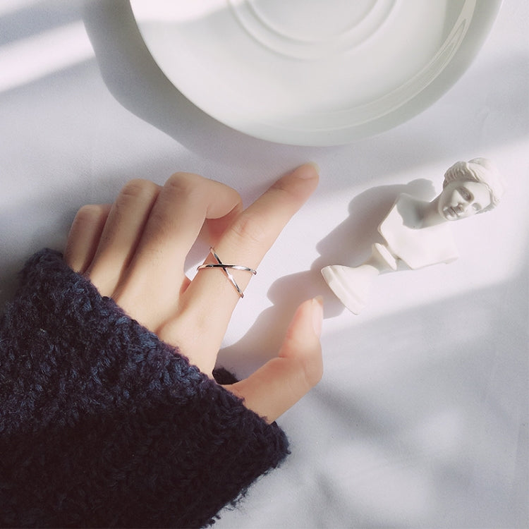 Open cross silver tone ring worn on finger, thin band with cross cutout.