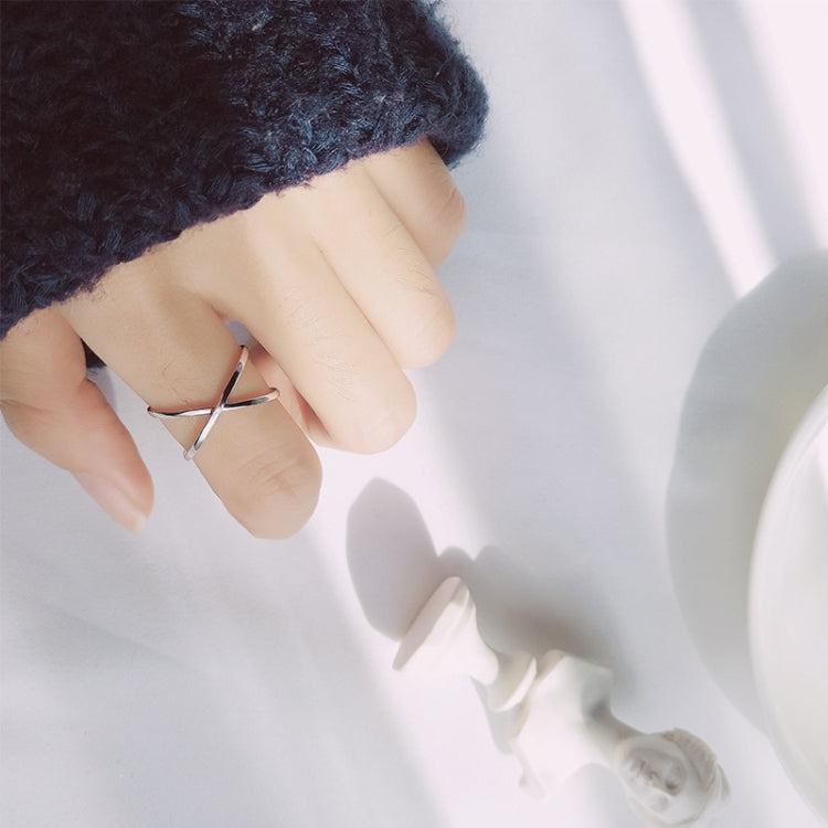 Close-up of polished open cross ring on finger, slim silver tone band.