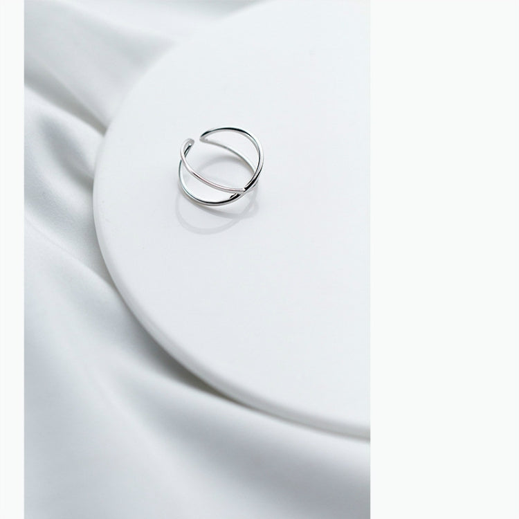 Polished sterling-silver tone open cross ring, thin band on white fabric.