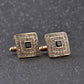 Gold-tone square cufflinks with black center and clear rhinestone border on bar