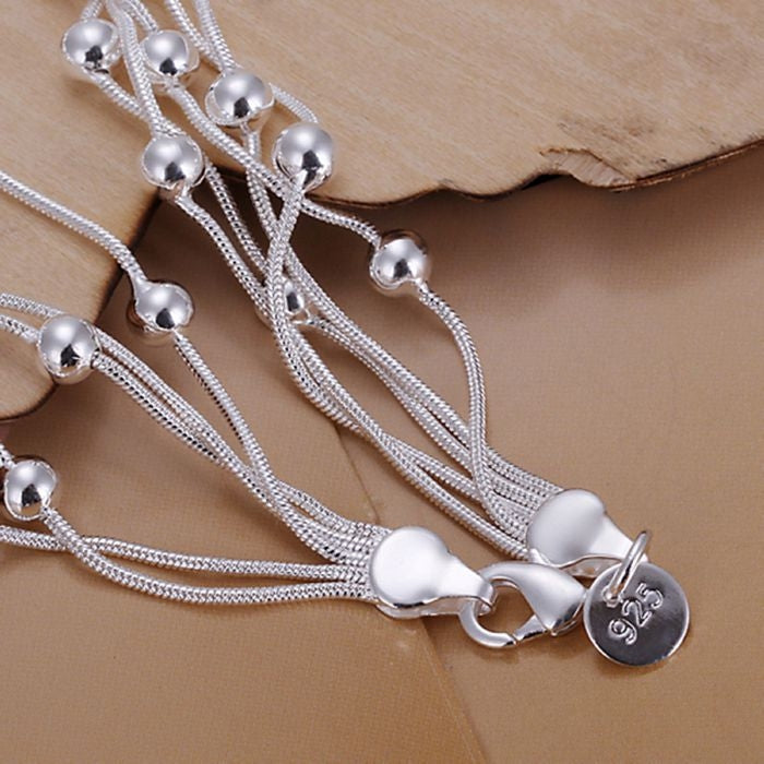 Silver plated bracelet detail: layered cords with spherical beads and round 925 tag charm