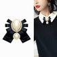 Bow brooch worn on a white-collared top: black ribbon with oval pearl and rhinestones