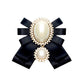 Black satin bow brooch with oval pearl centerpiece, rhinestone accents, and small pearl pin