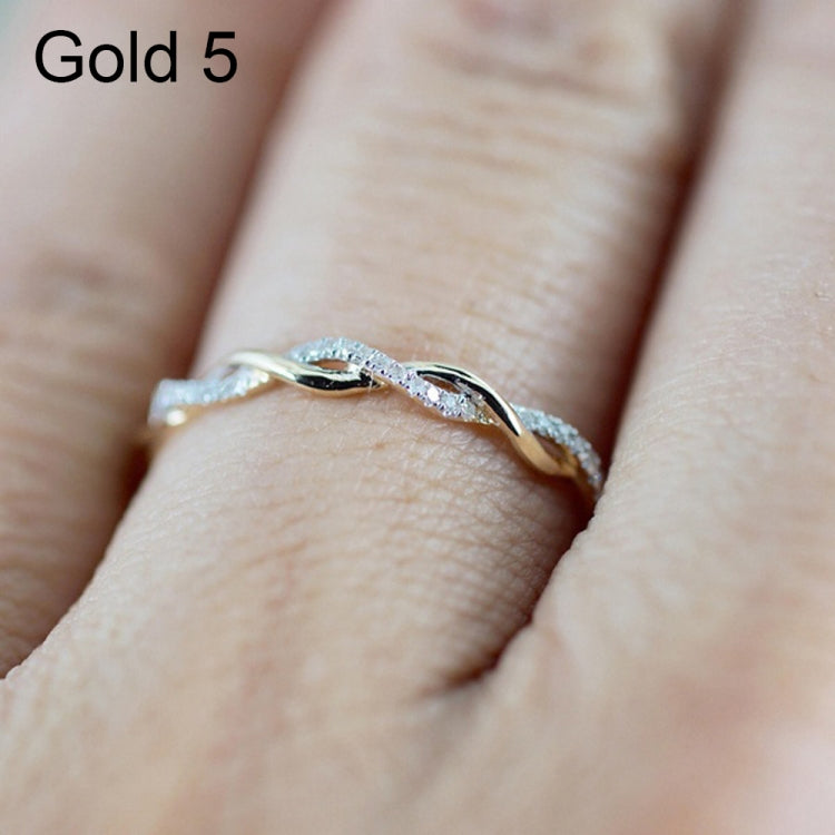 Twist-style cubic zirconia ring on finger, gold-toned metal with small round stones.
