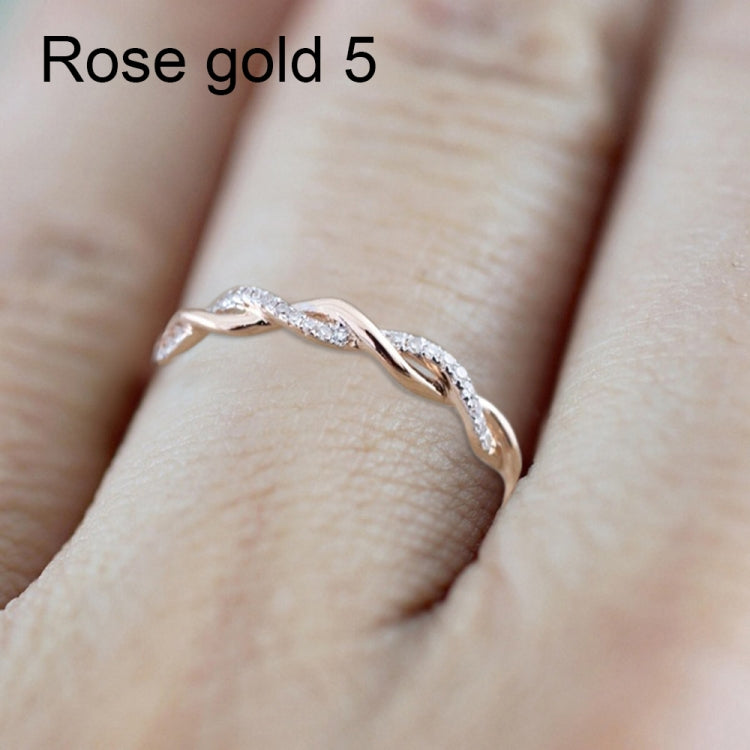 Twist-style cubic zirconia ring on finger, rose-gold toned metal with round stones.