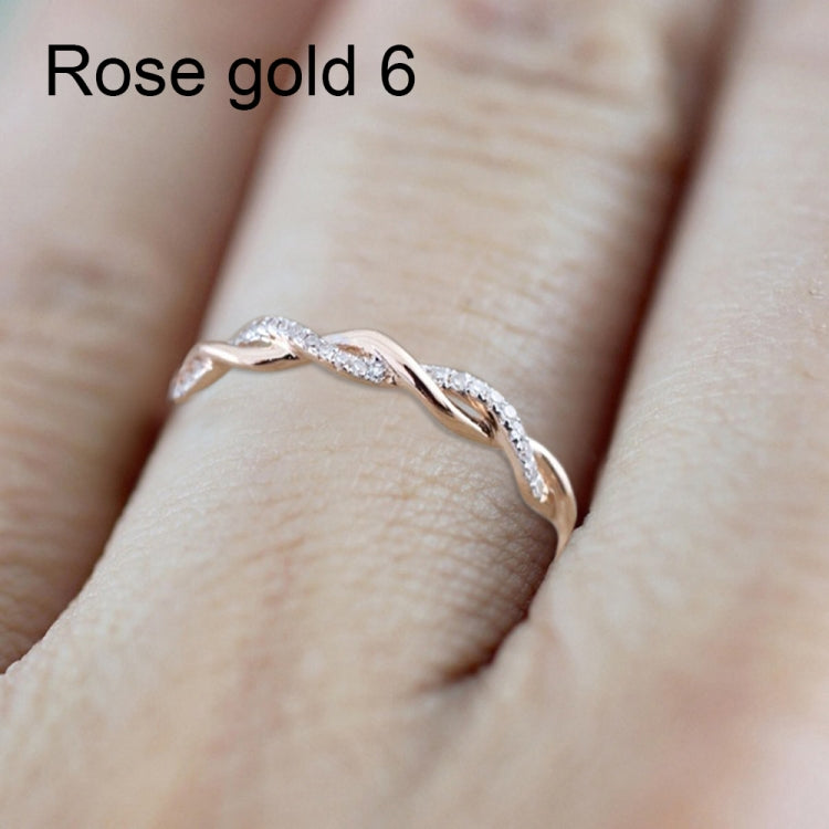 Twist-style cubic zirconia ring on finger, rose-gold toned metal with sparkling round stones.