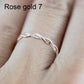Twist-style cubic zirconia ring on finger, rose-gold toned metal with round sparkling stones.