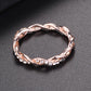 Rose gold twisted band ring with cubic zirconia oval accents, close-up on dark surface