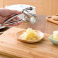 Hand-held stainless rotary cheese grater on a cutting board with shredded cheese