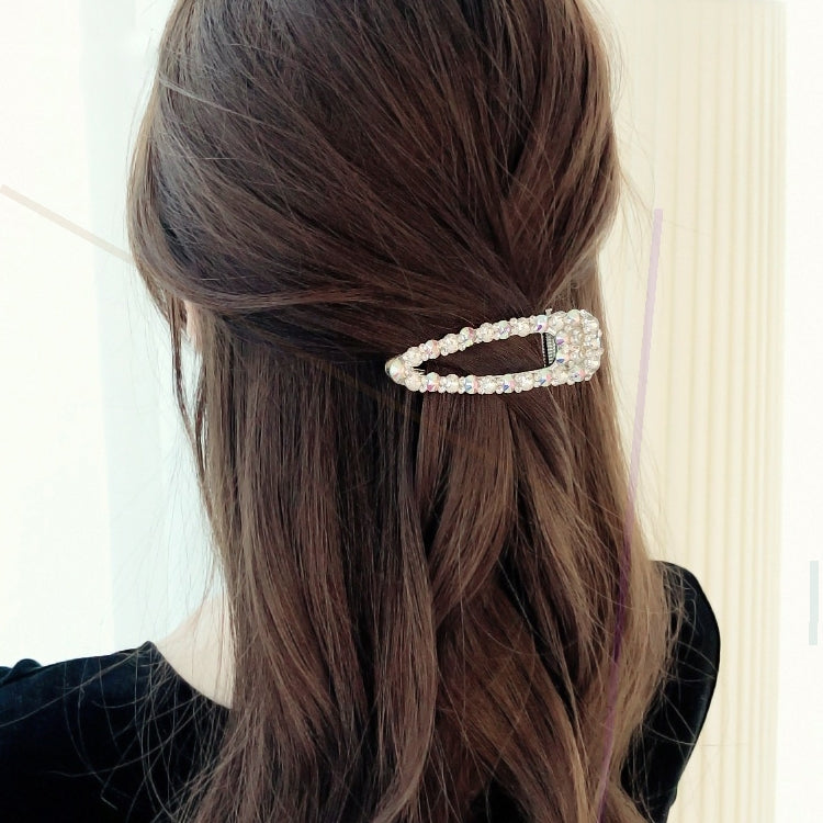 Crystal and faux pearl hair barrette clipped on dark hair, rectangular frame style