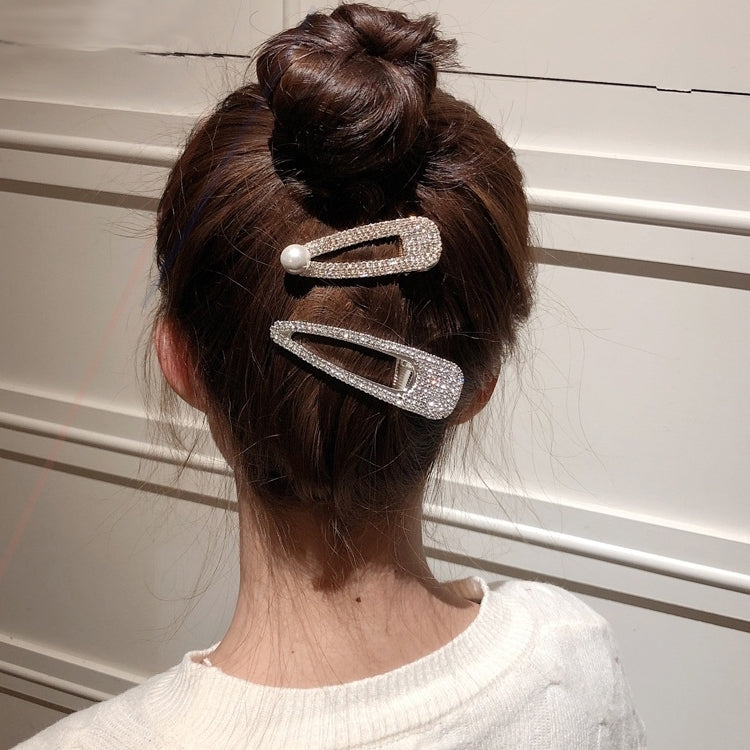 Two rhinestone hair barrettes with pearl accent on a bun hairstyle