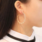 Gold-tone crystal hoop earring on ear, open teardrop shape