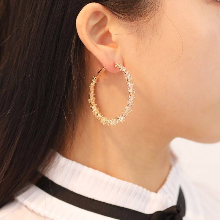 Gold-tone crystal hoop earring on ear, open teardrop shape