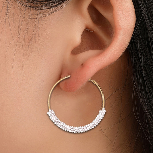 Gold-tone hoop earrings with white bead fringe, close-up on ear