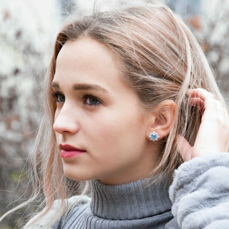 Blue gemstone snowflake stud earrings on a woman’s ear, silver-toned with clear crystals.