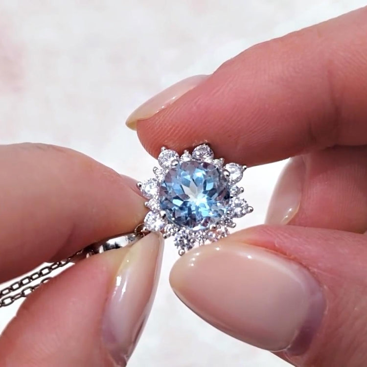 Close-up of silver ring with bright blue oval gemstone and snowflake crystal halo.