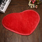 Red heart-shaped bath mat with plush shag pile and non-slip edge binding.