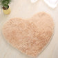 Beige heart-shaped bath mat with fluffy shag texture and non-slip edge trim.