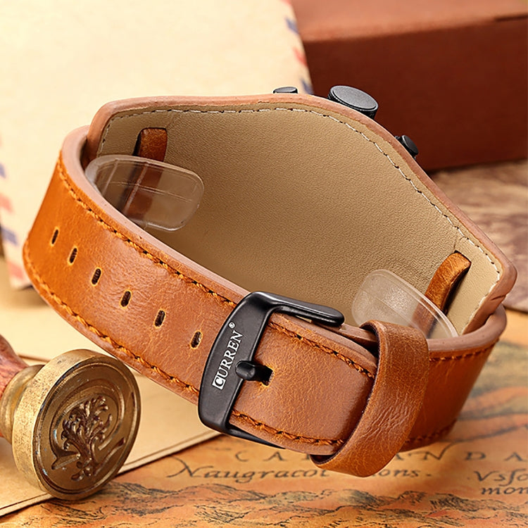 Leather watch strap close-up with orange-brown pin buckle and perforated keeper holes.