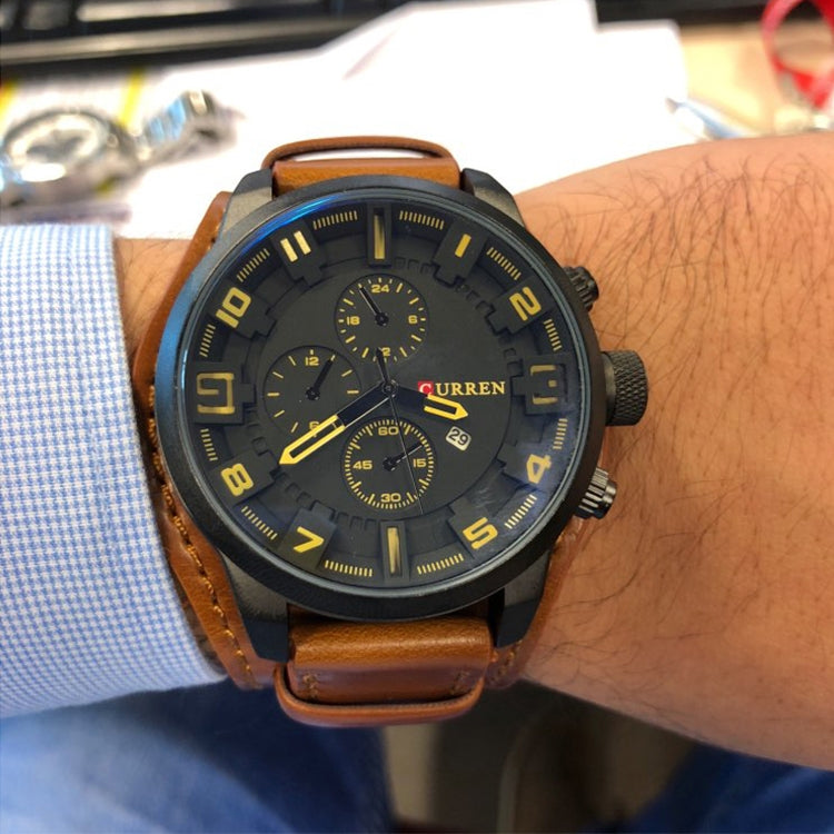 Men's quartz watch on wrist with brown leather band and black dial, yellow markers and subdials.