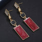 Long gold-tone drop earrings with red marbled rectangles and black squares between links