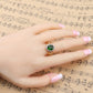 Hand wearing gold oval green gemstone ring with round clear stones on halo