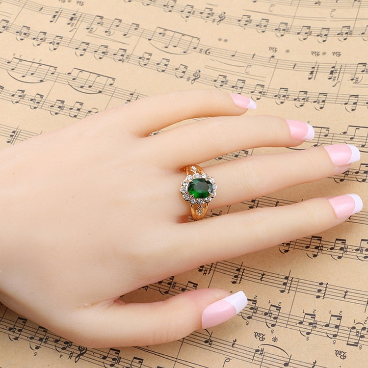 Hand wearing gold oval green gemstone ring with round clear stones on halo
