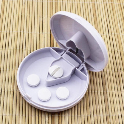 Round white plastic medicine dispensing box with lid open, showing compartments and blade