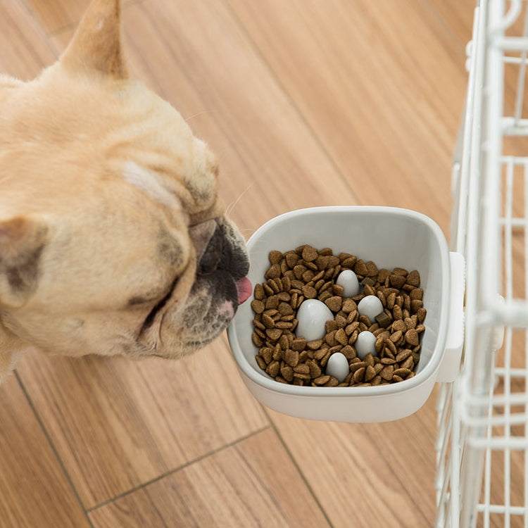 White plastic anti-choke hanging pet bowl with kibble, attached to cage side