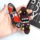Mini finger skateboard deck with red/black graphics and yellow wheels in a hand