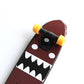 Mini finger skateboard close-up: black truck, yellow wheels, brown and black graphic deck