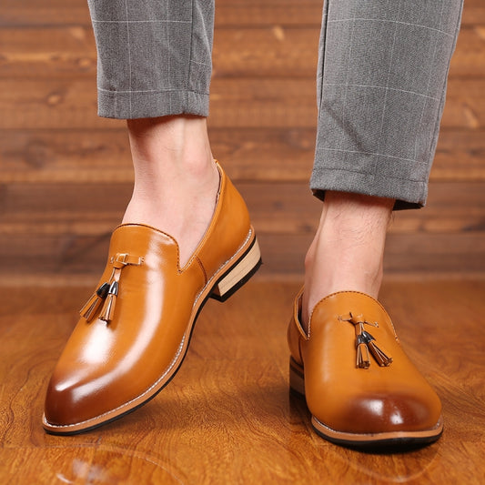 Men's pointed tan dress shoes on feet, tassel accents and low stacked heel