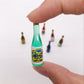 Mini wine drink bottle ornament held between fingers, mint green glass bottle shape.