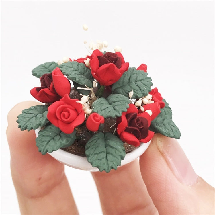 Miniature potted rose bouquet close-up held by fingers, with red roses and green leaves