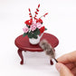 Mini chicken-hair simulation brush toy resting on red round table beside flower bouquet