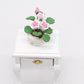 Mini potted rose ornament with pink-and-white flowers and green leaves on a white stand