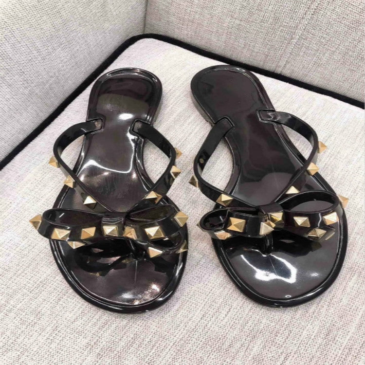Black flat thong sandals with rhinestone bow detail across the straps