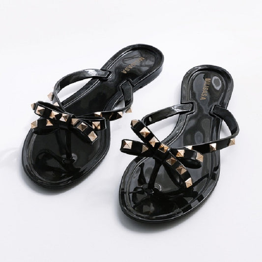 Black flip-flops with rhinestone-studded bow straps and thong-style flat sole