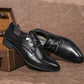 Black pointed-toe lace-up dress shoes shown at angle on a tabletop