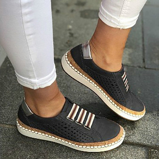 Black slip-on sneakers with perforated upper, striped strap detail, and cushioned sole