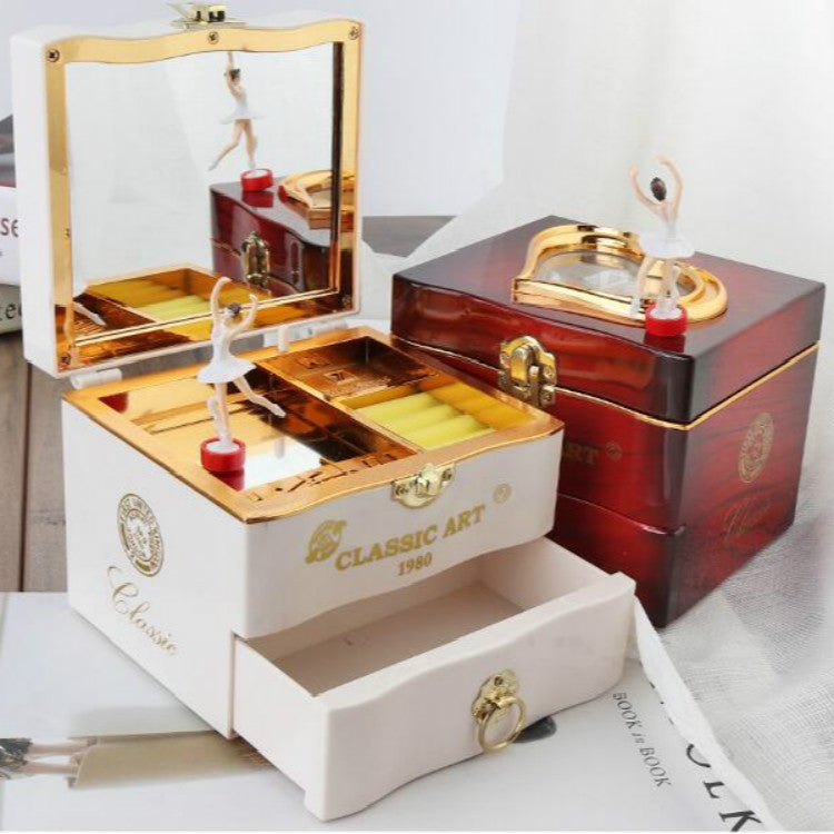 Open white music box with compartment tray and gold-framed dancer, beside a red box