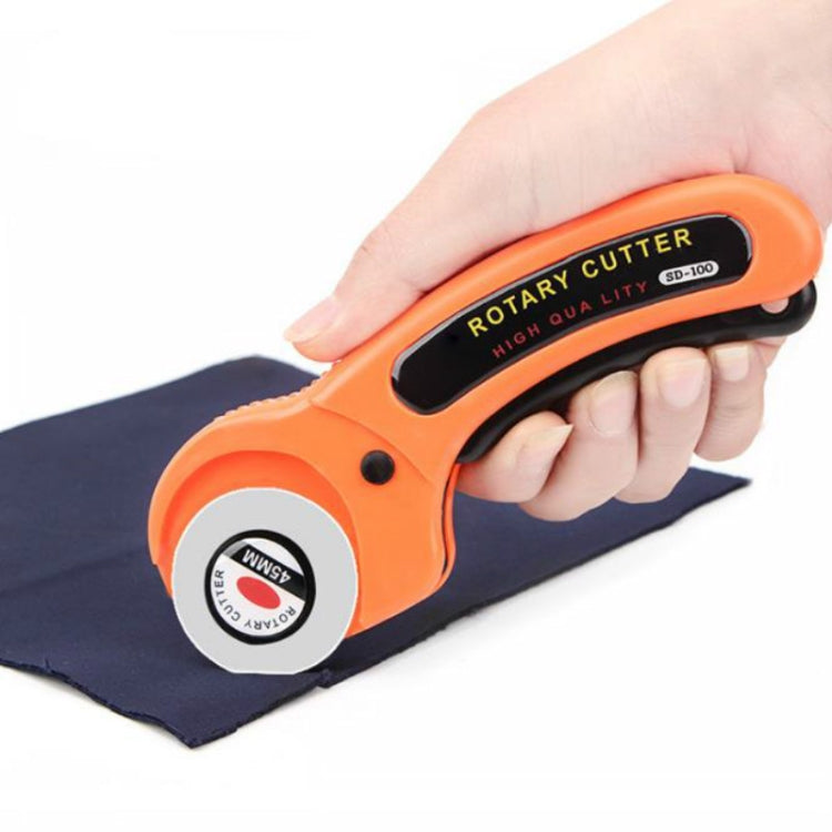 Orange rotary cutter with round blade, held cutting dark fabric cloth for sewing