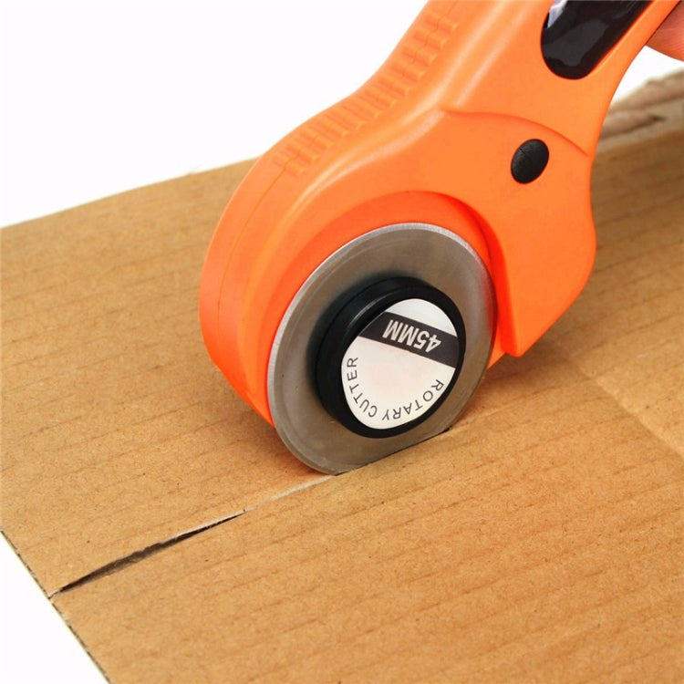 Orange rotary cutter rolling a round blade on cardboard surface