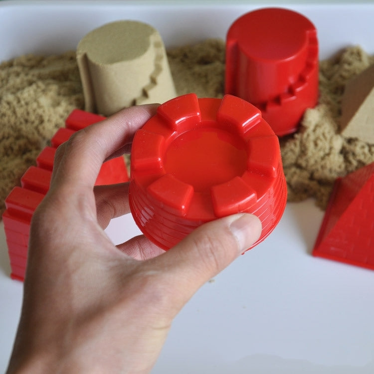 Hand holding a red round castle sand mold in a tray of play sand