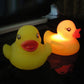 Two LED rubber duck bath toys, yellow and orange ducks glowing in dark water